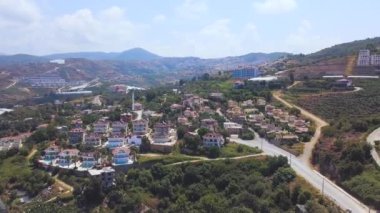 Stunning aerial view of the houses on the hill with blue cloudy sky on the background. Art. Cottages and villas located on the slope of green forested mountain.