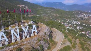 Arka arkaya Türk bayrakları ve dağ yamacında Alanya 'yı seviyorum yazan turizm konsepti. - Sanat. Yeşil bitki örtüsü ve çatıları olan harika bir ülke..