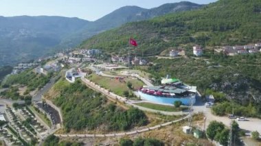 Dağların ve şehrin arka planında dalgalanan Türk bayrağı. - Sanat. Güneşli bir yaz gününde sallanan güzel bayrak manzarası, tatil beldesi ve turizm konsepti.