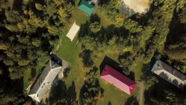 Uitzicht op het bos vanuit de lucht in de zomer in het moderne contryside gebied met prachtige huizen, groene bomen en de rivier. Voorraadbeelden. Bovenaanzicht van gebouwen daken, houten pier en rustige rivier. — Stockvideo