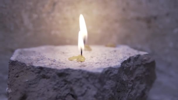 Primer plano de una vela encendida en una antigua iglesia. Filmación. Cerrar hermosas velas quemadas sobre fondo de pared gris oscuro — Vídeo de stock