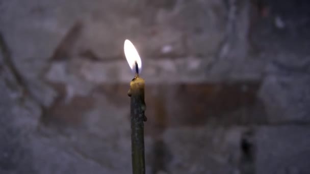 Primer plano de una vela encendida en una antigua iglesia. Filmación. Cerrar hermosas velas quemadas sobre fondo de pared gris oscuro — Vídeo de stock