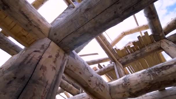 Blick von unten in das unfertige Holzhaus aus Rundhölzern auf blauem wolkenverhangenem Himmel. Clip. Schreinerarbeiten, Bau eines neuen Eigenheims. — Stockvideo