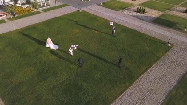 Velmi šťastní novomanželé běhají na zelené trávě pod slunečními paprsky v jejich svatební den baví během focení se svými malými dětmi. Umění. Koncept rodiny a lásky. — Stock video