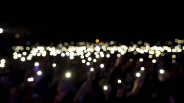 Karanlıkta ışıklar sallanırken salondaki odaksız seyirciler. Başla. Seyirciler konser sırasında ellerinde parlayan el fenerleriyle telefonlar, romantik atmosfer.