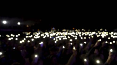 Karanlıkta ışıklar sallanırken salondaki odaksız seyirciler. Başla. Seyirciler konser sırasında ellerinde parlayan el fenerleriyle telefonlar, romantik atmosfer.