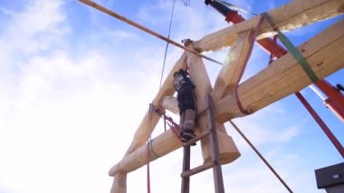 Büyük bir evin çatısında çalışan bir marangozun arka görüntüsü. Şarjör. Mavi bulutlu arka planda merdivenlerin üzerinde duran bir inşaatçının alt görünümü.