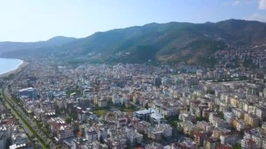 Yüksek yeşil dağlı bulutların önündeki tatil köyü manzarası. - Sanat. Yüksek binaları, otelleri ve parkları olan güneydeki sahil şehrinin havası..