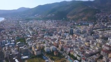 Yüksek yeşil dağlı bulutların önündeki tatil köyü manzarası. - Sanat. Yüksek binaları, otelleri ve parkları olan güneydeki sahil şehrinin havası..