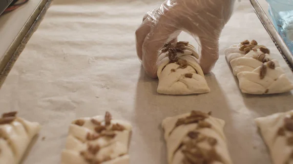 Zbliżenie cukiernicze ręce wprowadzenie niegotowane bułki z orzechami na tacy piekarnika. Materiał filmowy. Piekarz przygotowuje słodkie i smaczne wyroby cukiernicze. — Zdjęcie stockowe