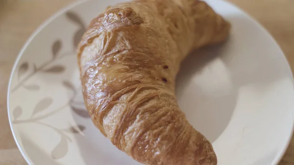 Top view of tasty fresh croissant lying on the white glass plate, french breakfast concept. Stock footage. Close up of beautiful pastry product on the wooden surface. — Stock Photo, Image