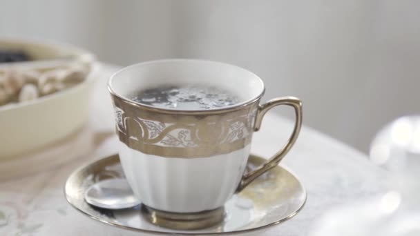 Närbild av elegant porslin kopp varmt te med ånga stående på bordet i ljust rum. Lagerbilder. Aristokratisk morgonfrukost. — Stockvideo