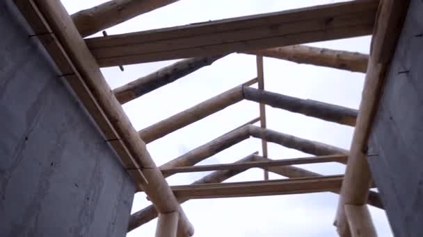 Vista inferior del sistema de armadura de madera, construcción del techo de la casa sobre el fondo nublado del cielo. Clip. Techo inacabado y dos muros de hormigón y el sitio de construcción . — Vídeo de stock