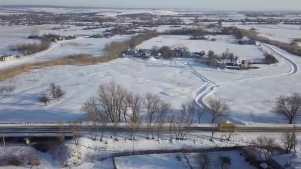 Aerial of the winter road with a bus riding along the small village covered by snow. Shot. Winter landscape with wooden houses, road and moving yellow bus. — Stock Video