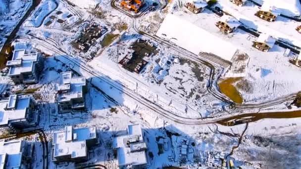 Flying over the industrial area of the city covered by snow on a sunny winter day. Journey. Aerial of beautiful houses and the construction site in winter time. — ストック動画
