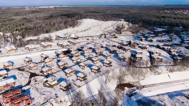 Aerial view of winter village near the pine tree forest. Journey. Amazing flight above houses and cottages covered by snow located in ecological area. — ストック動画