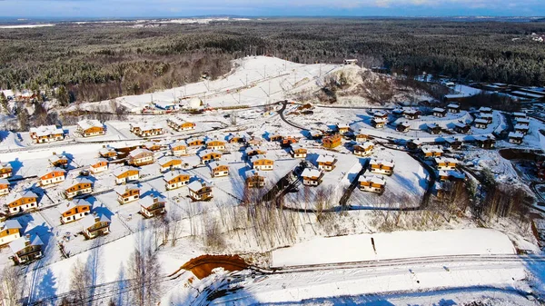Letecký pohled na zimní vesnici v blízkosti borového lesa. Cesta. Úžasný let nad domy a chalupami pokryté sněhem se nachází v ekologické oblasti. — Stock fotografie