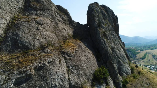 Aérea de gran relieve de rocas entre el espeso bosque verde que crece en el valle. Le dispararon. Primer plano del pico de montaña cubierto por musgo verde con campo verde detrás . — Foto de Stock