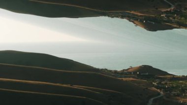 Aerial view of surreal with green hills and small town located near the sea against blue sky with the mirror effect. Shot. Abstract reflection