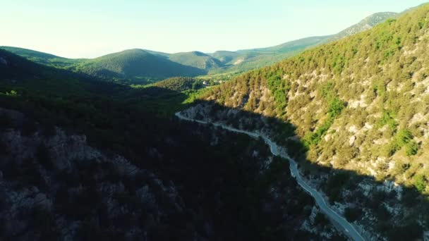 Aerial view of the road between high mountains covered with green trees and shrubs against blue sky in sunny summer day. Shot. Beautiful colorful landscape. — стоковое видео