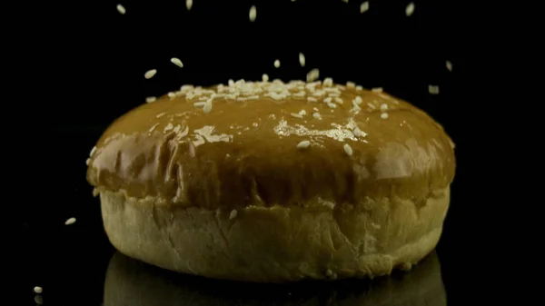 Detailní záběr bílých sezamových semínek padajících na čerstvou hamburgerovou housku izolovanou na černém pozadí, jídlo a koncepci přípravy. Záběry ze skladu. Mnoho sezamových semen, asijská kuchyně. — Stock fotografie