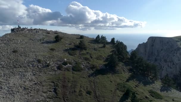 Mavi deniz kıyısındaki dik uçurumun nefes kesici hava manzarası. Teleferikli araba ve bulutlu arka planda yürüyen insanlar. Vuruldu. Dağ yamacında füniküler, ulaşım konsepti. — Stok video