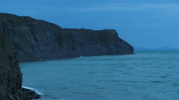 Impresionante paisaje marino con un acantilado empinado sobre fondo de cielo azul oscuro. Le dispararon. Tarde en el mar con pequeñas olas y rocas . — Vídeo de stock