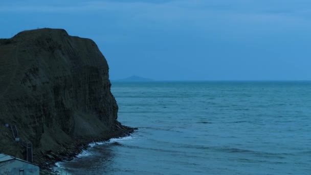 Splendido paesaggio marino con una ripida scogliera su sfondo cielo blu scuro. Gli hanno sparato. Serata al costo del mare con piccole onde e rocce . — Video Stock