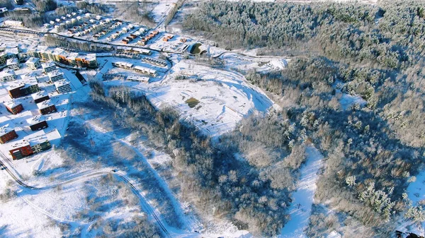 Campo en el día de invierno nevado, vista aérea de pueblo rural y carretera en invierno. Moción. Vista aérea del bosque de pinos y pequeñas casas cerca del lago . — Foto de Stock