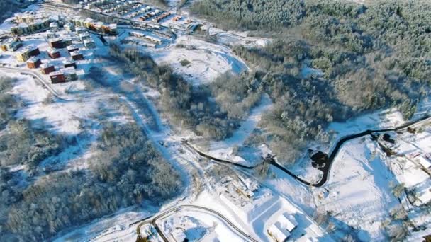 Platteland op besneeuwde winterdag, luchtfoto van landelijk dorp en weg in de winter. Beweging. Uitzicht vanuit de lucht op dennenbossen en kleine huisjes bij het meer. — Stockvideo