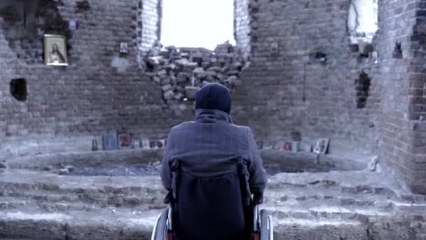 Vue arrière d'un homme en fauteuil roulant pour handicapés dans l'église en ruine. Des images. Le concept de perte — Video