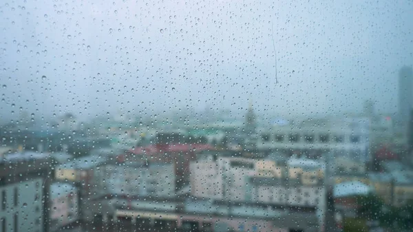 La pluie tombe sur un verre avec un fond. Images d'archives. Des gouttes de pluie sur la fenêtre sur le fond de la ville — Photo