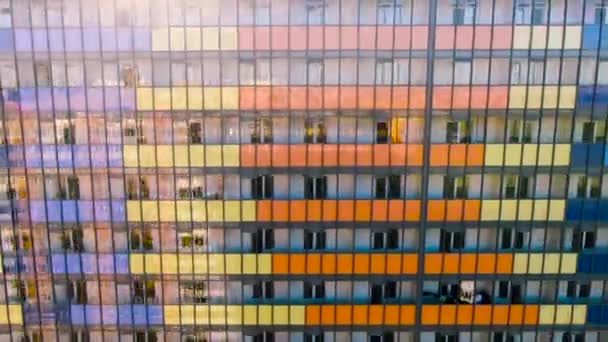 Flygfoto av glödande fönster i flervåningshus med återspegling av staden. Rörelse. Flyger längs den färgglada glasfasadbyggnaden och balkonger under den skinande solen. — Stockvideo