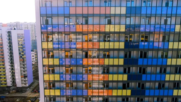 Vista aérea de janelas brilhantes do edifício de vários andares com o reflexo da cidade. Moção. Voando ao longo do edifício colorido fachada de vidro e varandas sob o sol brilhante . — Fotografia de Stock