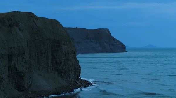 Marina deslumbrante com um penhasco íngreme no fundo do céu azul escuro. Atingido. Noite ao custo do mar com pequenas ondas e rochas . — Fotografia de Stock