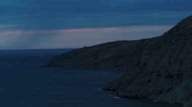 Yağmurlu bir akşamda Pasifik Okyanusu 'ndaki dağ kayaları. Vuruldu. Okyanus yüzeyinin üzerindeki yağmur bulutları, yeşil tepeli nefes kesici manzara..