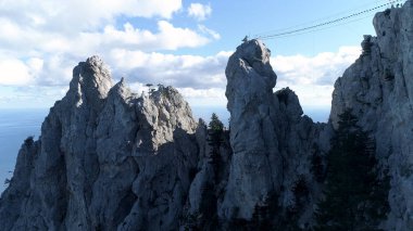 Mavi okyanus ve arka planda bulutlu gökyüzü olan dağ zirvesindeki asma köprü. Vuruldu. Kayaların üzerinde halat köprüsü olan deniz kıyısının inanılmaz hava manzarası..