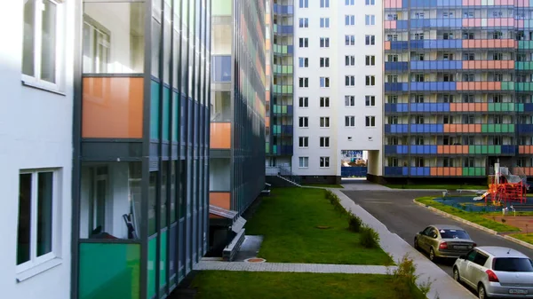 Colorful playground inside the yard surrounded by new residential houses. Motion. Bright building with colorful balconies and green lawn.