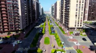 Güzel şehir caddesinin havadan görünüşü güneş ışığının altında bir sürü yürüyen insan ve araba sürüyor. Hareket. Evlerin, binaların, yol boyunca yeşil çimlerin üzerinde uçuyor..