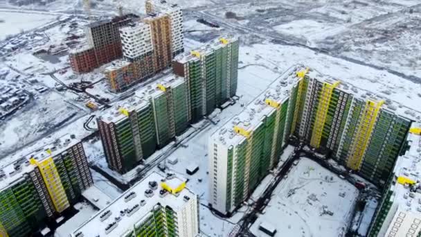 Vista in alto della città in inverno al tramonto su sfondo campo innevato. Mozione. Veduta aerea drone di edifici alti verdi e gialli, zona notte della città . — Video Stock