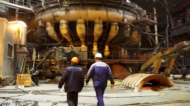 Visão traseira de metalúrgicos andando dentro da loja quente da planta de produção metalúrgica. Imagens de stock. Conceito da indústria pesada, trabalhadores na fábrica . — Vídeo de Stock