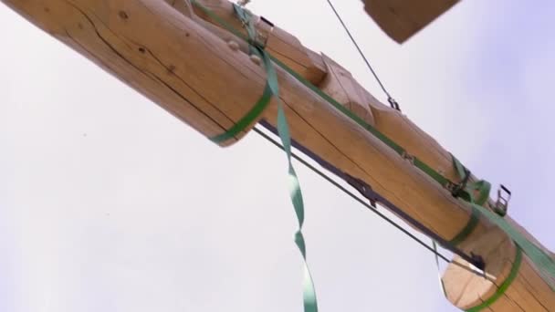 Bottenvy av trä stockar, delar av takkonstruktionen bärs av kranen och grönt rep på blå molnig himmel bakgrund. Klipp. Snickeriarbetskoncept. — Stockvideo