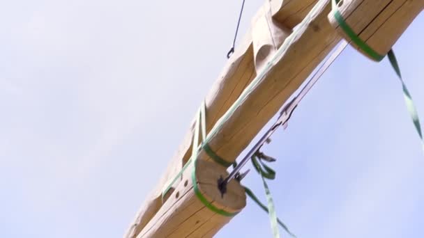 Blick von unten auf den Kranmechanismus, der den Baumstamm vor blauem wolkenverhangenem Himmel hebt. Clip. Kran mit Holz für den Bau eines Holzhauses. — Stockvideo