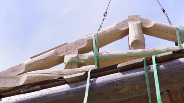 Bottenvy över kranen lyfta ett tak joist av nytt hus på byggarbetsplatsen. Klipp. Delar av ny ekologisk byggnad på blå molnig himmel bakgrund. — Stockvideo