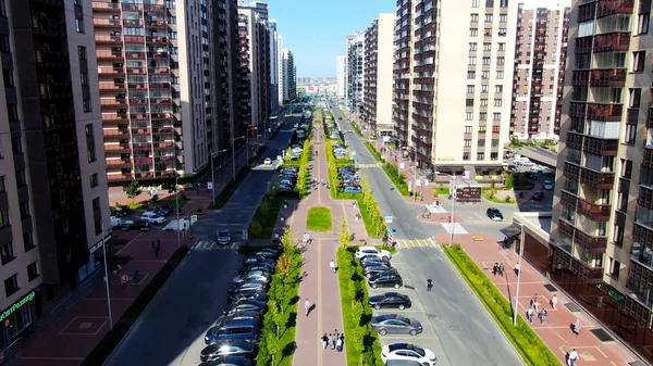 Aereo di persone che camminano lungo il vicolo verde nella strada estiva della città. Mozione. Volare lungo la strada con edifici, auto e sentiero . — Foto Stock