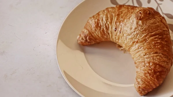 Primo piano di croissant appena sfornato sdraiato su un piatto di ceramica su sfondo bianco del tavolo. Filmati delle scorte. Concetto di prodotti da forno e alimentari . — Foto Stock