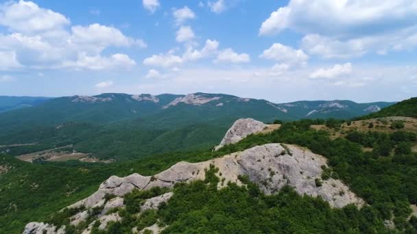 Αεροφωτογραφία των βράχων του βουνού με μια απέραντη κοιλάδα στο μπλε θολό φόντο του ουρανού. Πυροβολήθηκε. Φυσικό τοπίο που κόβει την ανάσα με πράσινα δέντρα, βράχους και λόφους. — Αρχείο Βίντεο