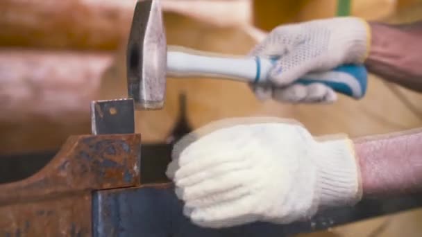 Arbeiter mit Schutzhandschuhen hämmern Metallkonstruktion auf Holzstämme Hintergrund. Clip. Schreinerarbeiten auf Baustelle. — Stockvideo