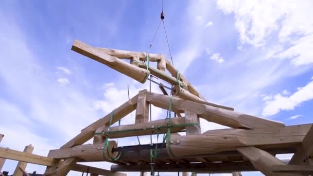 Crane above the new wooden building under construction on sunny day in the countryside area. Clip. Wooden log construction being transported above the house frame. — Stock Footage Crane above the new wooden building under construction on sunny day in the countryside area. Clip. Wooden log construction being transported above the house frame. Stock Footage