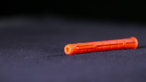 Close-up of orange plastic dowel. Stock footage. Single orange dowel lies on black background. Dowel is used in construction and repair work with screws for mounting in walls — 비디오